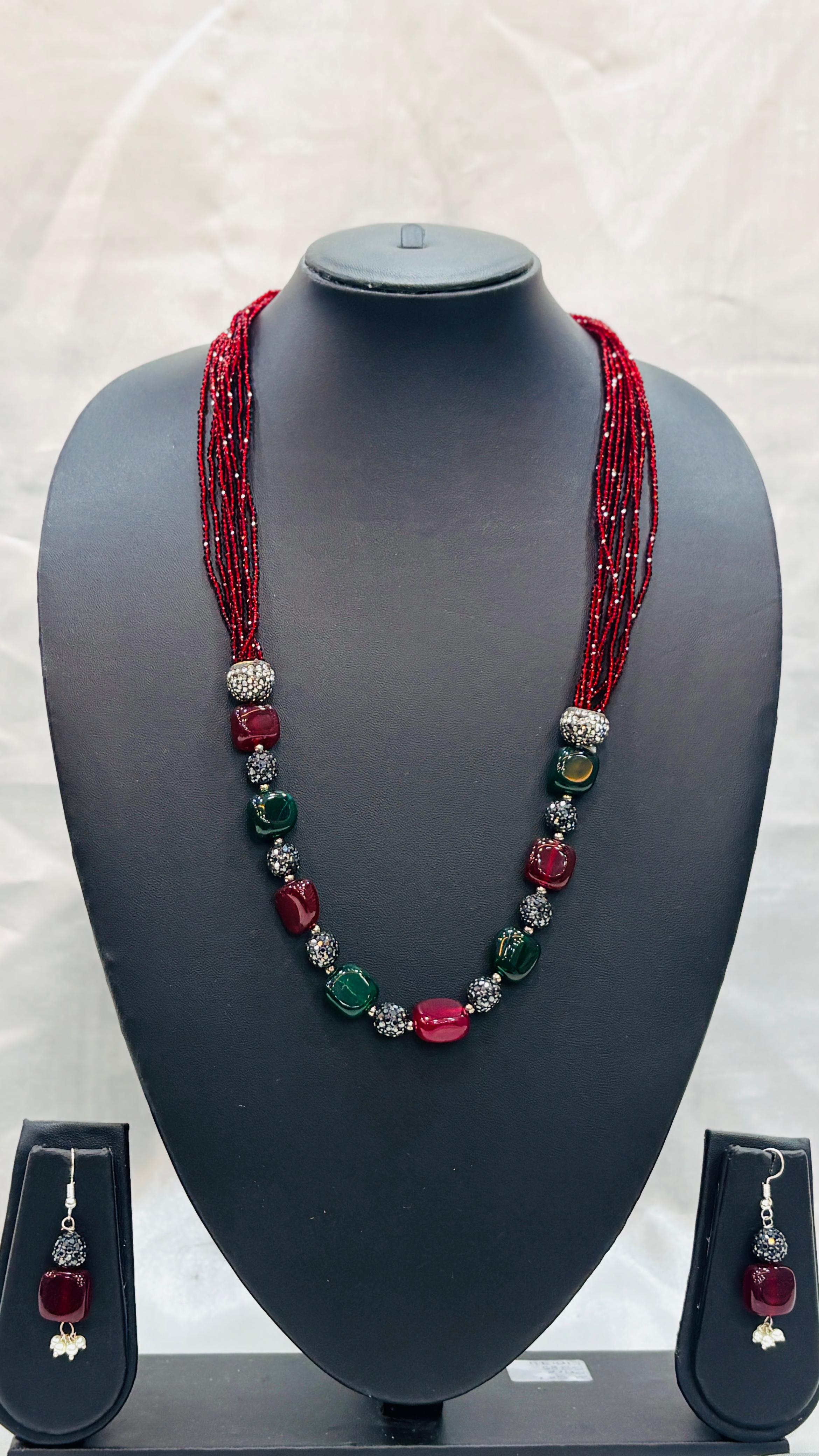 Necklace with red and green beads on a mannequin bust with matching earrings.
