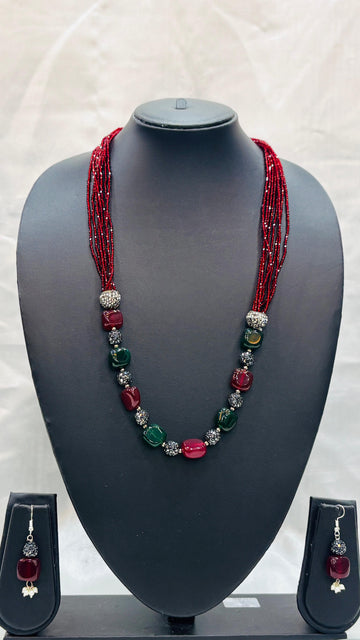 Necklace with red and green beads on a mannequin bust with matching earrings.