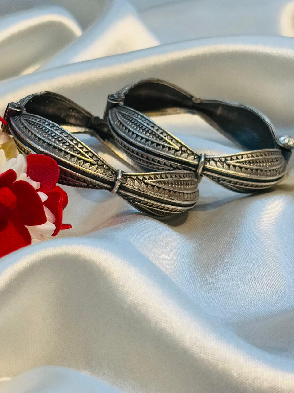 Silver bangles with intricate designs on a white fabric background