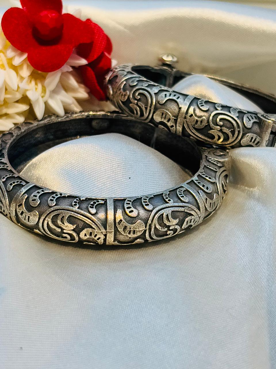 Decorative silver bangles on a white fabric background with red and yellow flowers.