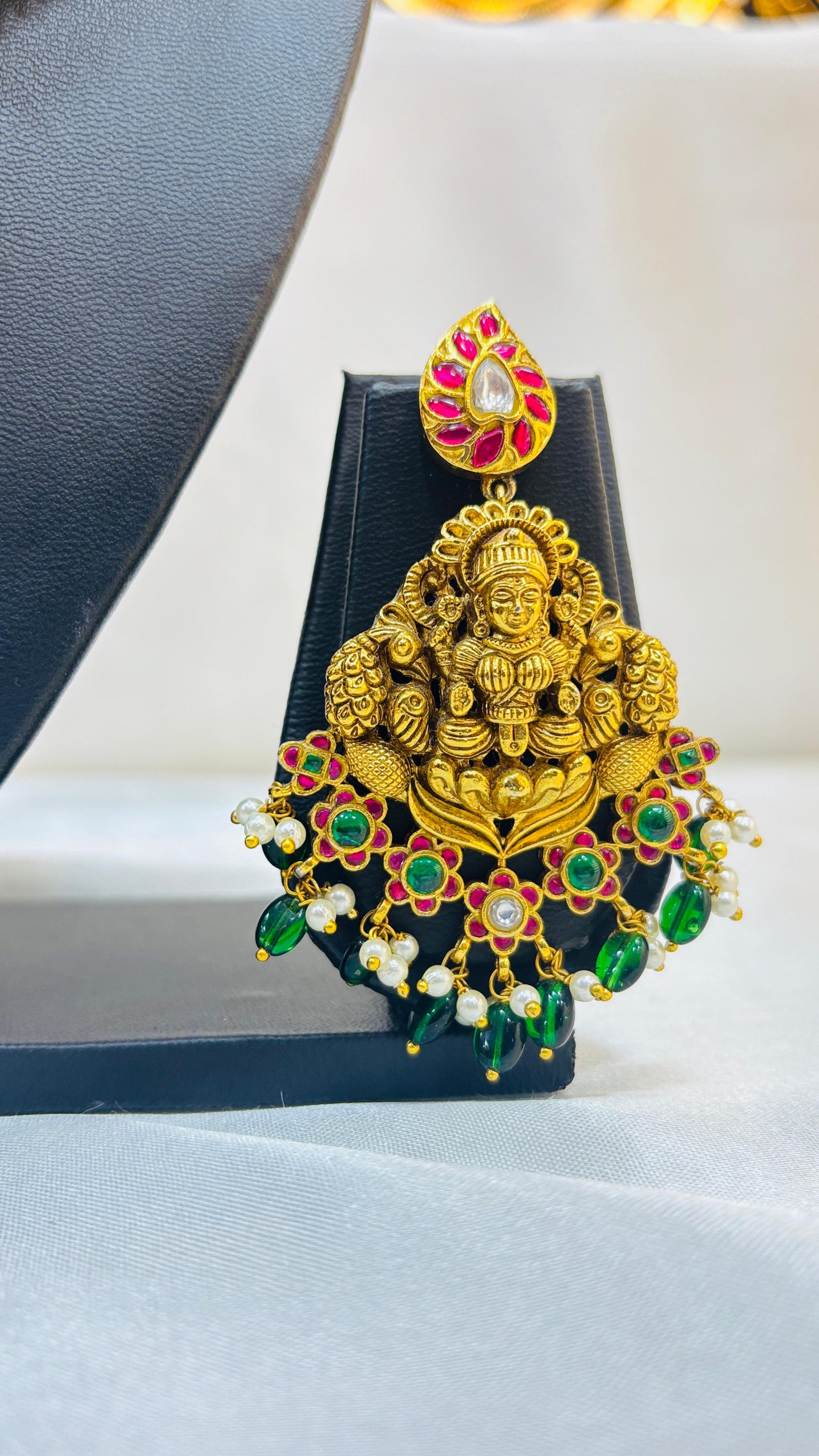 Decorative gold pendant with colorful stones on a black stand