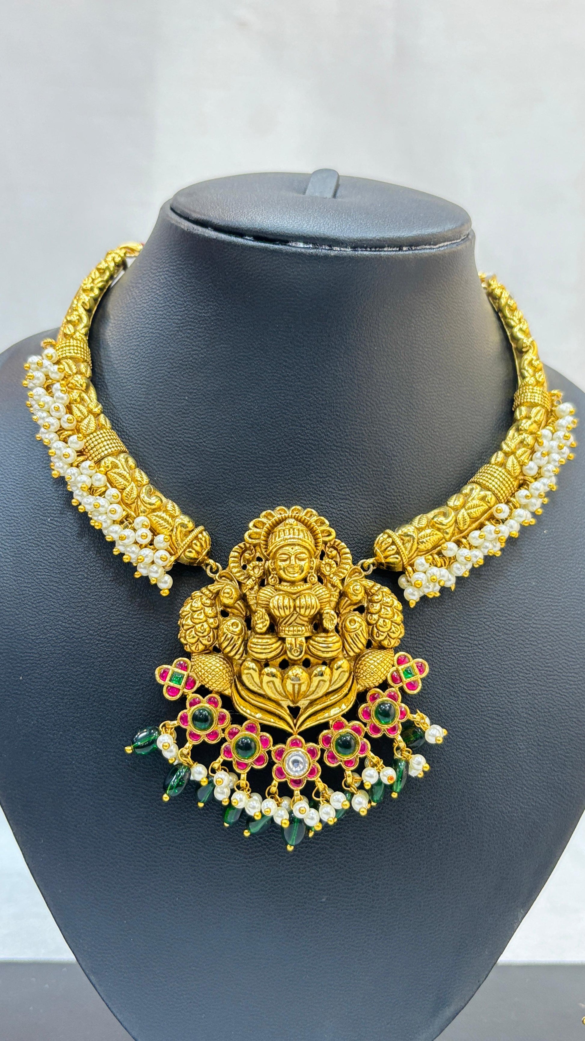 Gold necklace with a deity figure pendant on a mannequin bust.