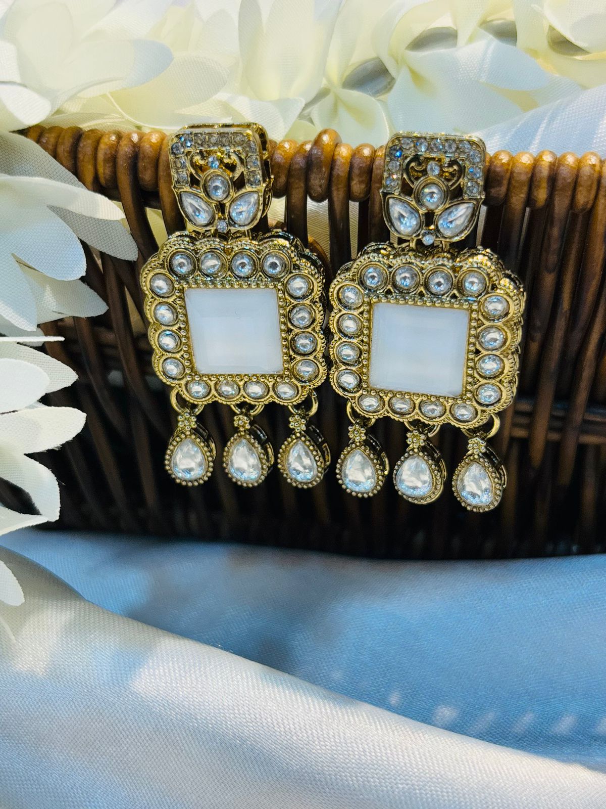Pair of earrings with White gemstones and gold accents on a black stand.