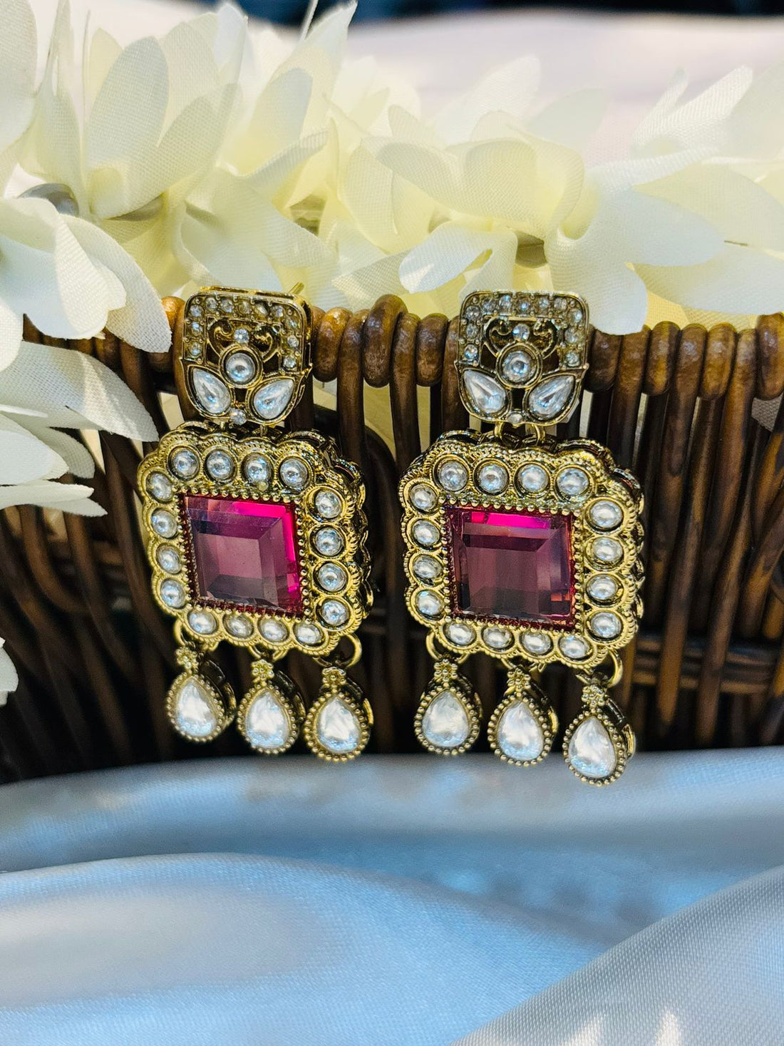 Pair of earrings with pink gemstones and gold accents on a black stand.