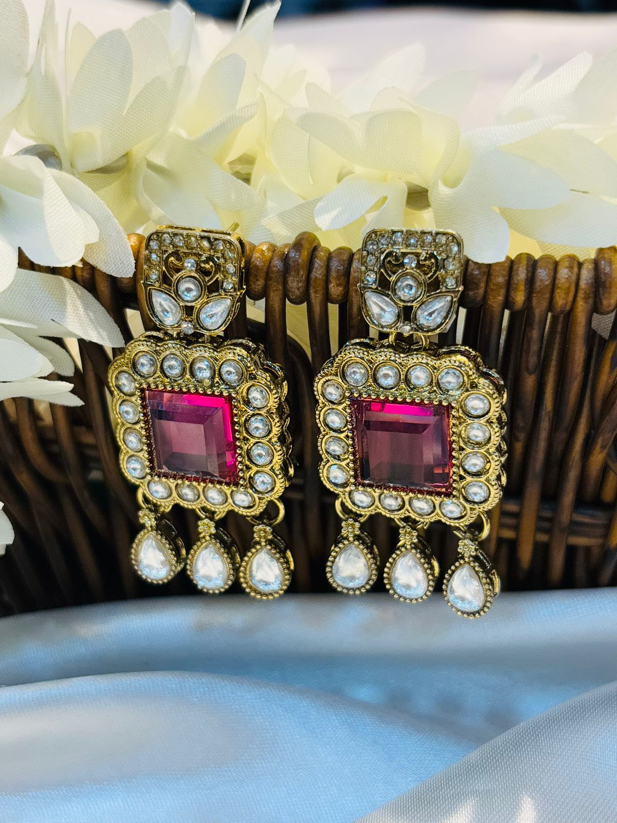 Pair of earrings with purple gemstones and gold accents on a black stand.