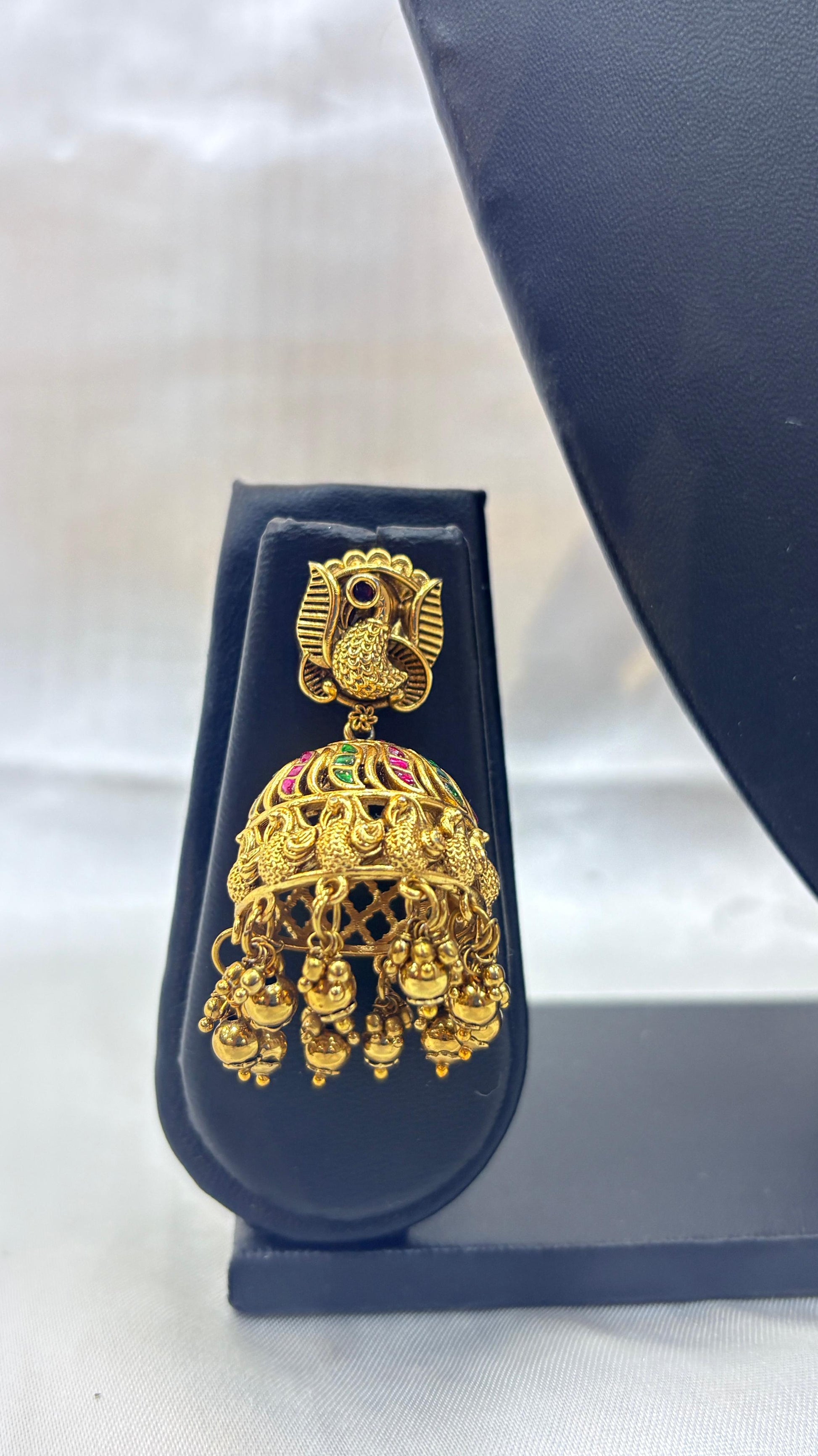 Gold earrings with green and red stones on a dark blue stand