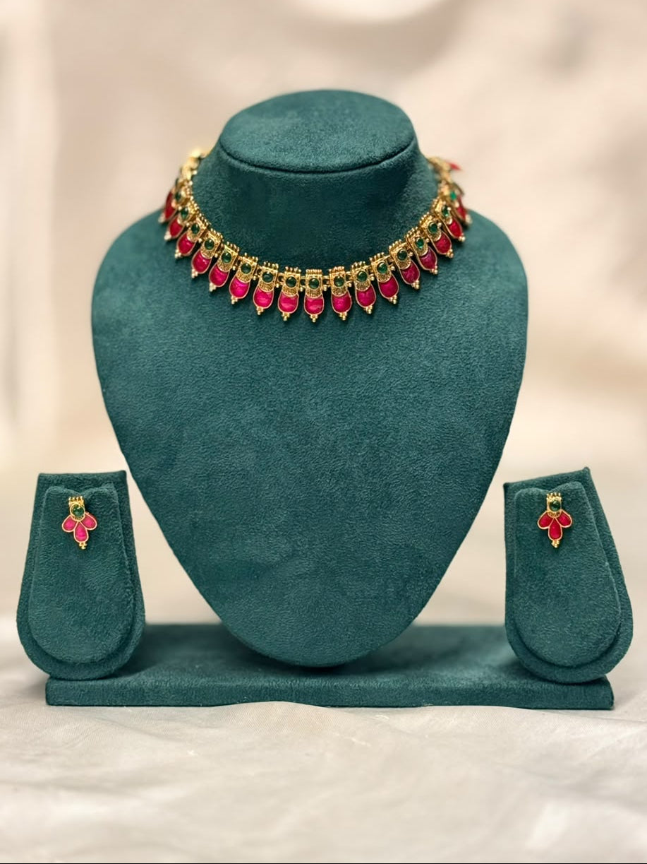Gold-plated jewelry set with a necklace and matching earrings, embellished with red stones, displayed on a teal velvet jewelry bust.